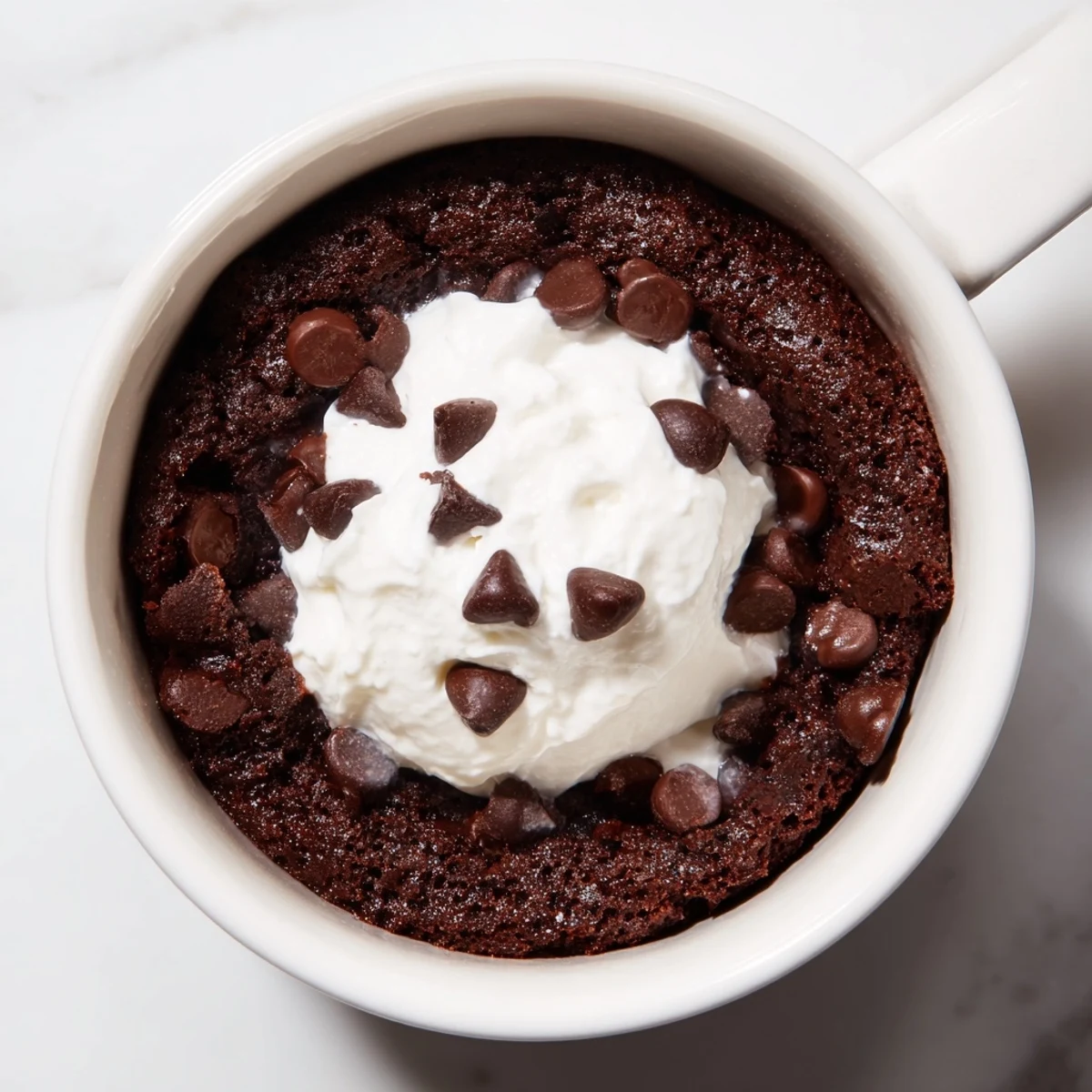 Steaming hot chocolate mug cake topped with whipped cream, ready for a sweet treat.