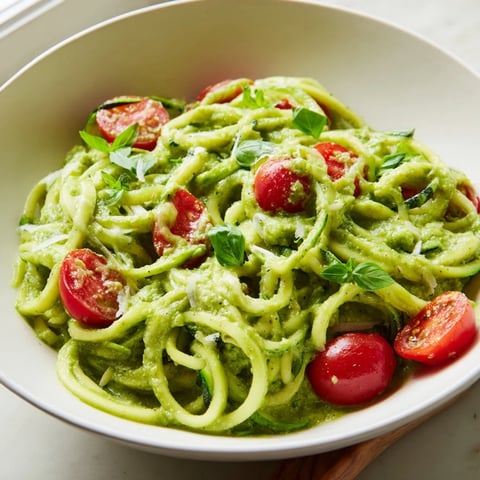 Creamy avocado pesto clings to tender zucchini noodles, with halved cherry tomatoes adding a juicy burst in this vibrant low-carb main dish.