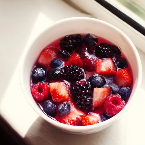 A vibrant Nature’s Cereal Bowl with fresh berries in chilled coconut water and ice, served on a wooden table.