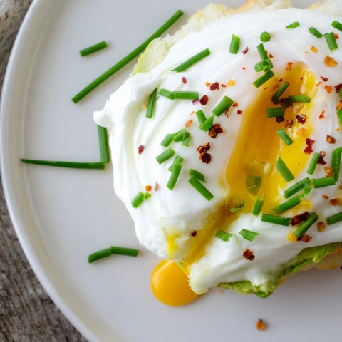 Golden-brown Cloud Bread Breakfast Clouds on a plate, topped with creamy avocado slices and a perfectly poached egg with a runny yolk.  