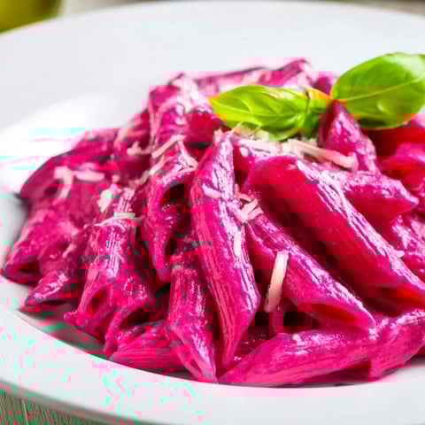 A vibrant bowl of Pink Pasta with Beet Cream, the silky beet sauce glazing penne with fresh basil and grated Parmesan garnish.