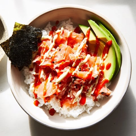 Flaky salmon and creamy avocado top a bowl of warm, seasoned rice in this Emily Mariko Salmon Rice Bowl, drizzled with spicy mayo and served with crispy seaweed sheets.  