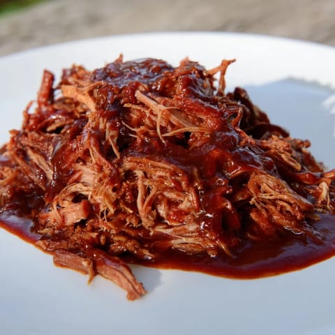 A close-up of tender 5-Ingredient BBQ Pulled Pork, swimming in rich barbecue sauce after cooking.
