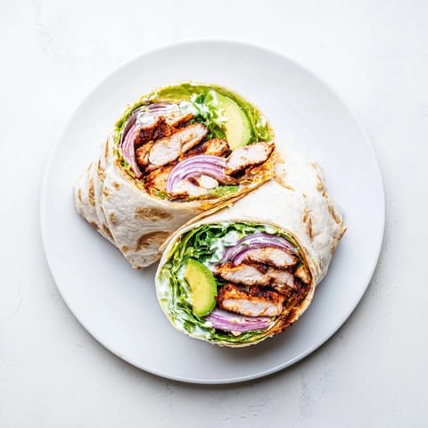 A vibrant platter of Smoky Chipotle Chicken Wraps topped with tangy Greek yogurt sauce, red onion, and diced tomatoes beside a lime wedge. 
