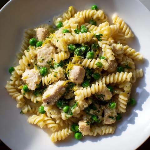 A close-up of the Garlic Butter Chicken & Pea Pasta, featuring tender chicken, bright green peas, and curly pasta coated in a creamy garlic butter sauce.  
