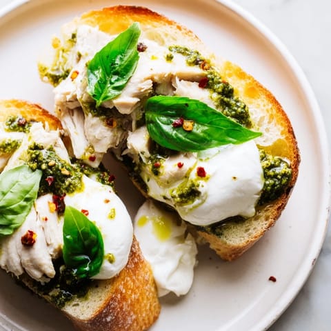 Crusty olive oil-brushed toast holds tender sliced chicken and a ball of burrata, drizzled with basil pesto for a delicious bite.