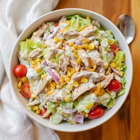 A hearty bowl of Ranch Chicken Chopped Salad, mixing sharp cheddar, cherry tomatoes, and cucumbers tossed in tangy, herb-filled ranch dressing.  