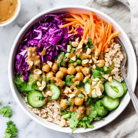 A close-up shot of a nourishing Peanut Chickpea Rice Bowl drizzled with creamy peanut dressing, garnished with fresh cilantro and scallions for added flavor.