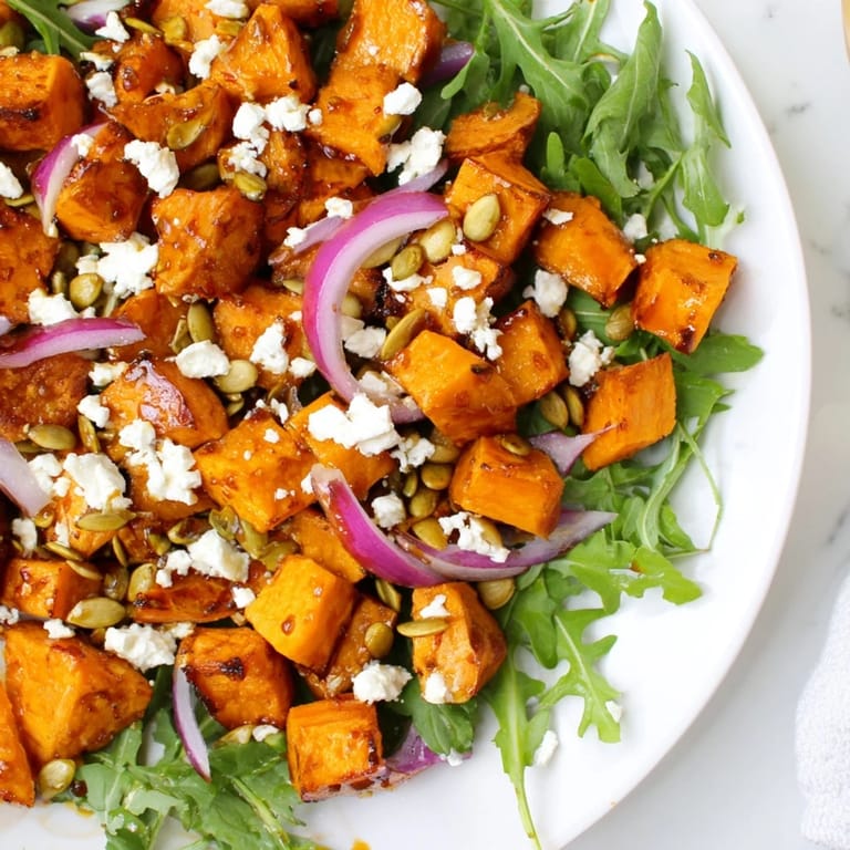 Colorful roasted sweet potato salad served on a white plate with red onion slices.