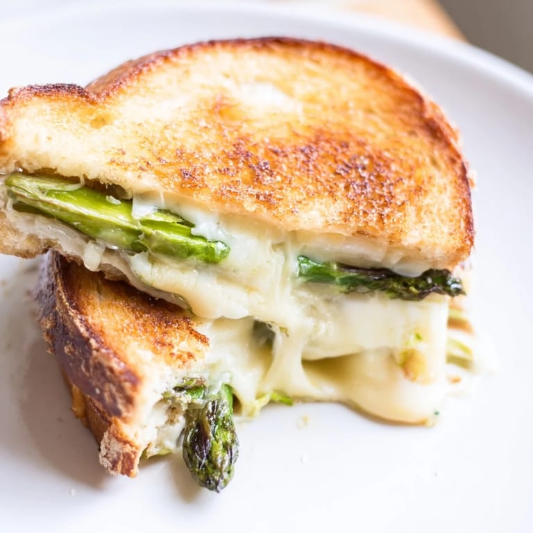 A close-up of Asparagus & Brie Grilled Cheese shows oozing cheese and tender green spears between crispy toasted bread.