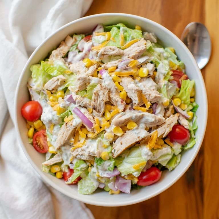 A hearty bowl of Ranch Chicken Chopped Salad, mixing sharp cheddar, cherry tomatoes, and cucumbers tossed in tangy, herb-filled ranch dressing.  