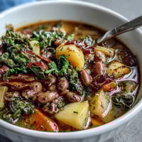 A steaming bowl of Soul Food Black-Eyed Pea and Collard Green Stew with tender greens and smoky broth.
